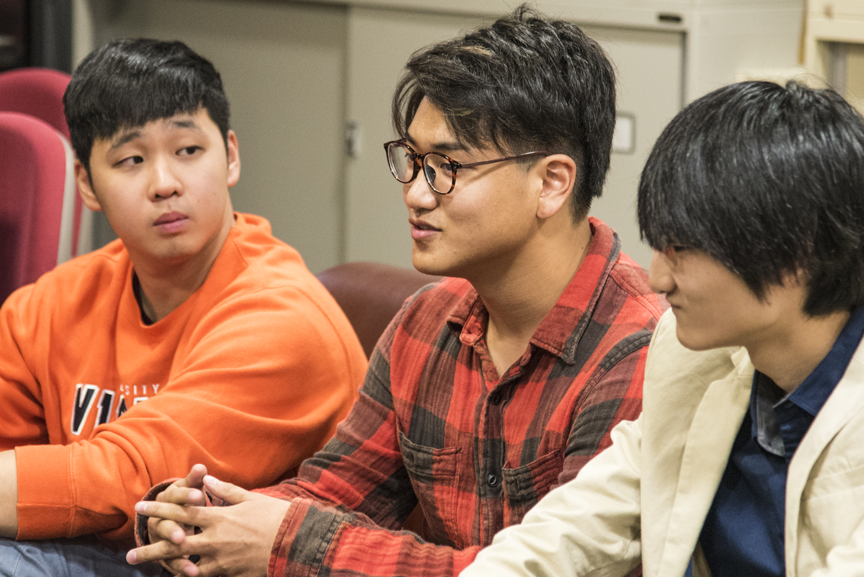 Three students sit on sofa and lean towards Dr. Kuno