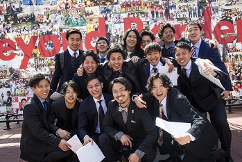 A group of students pose for a commemorative photo in front of the photo board outside on campus