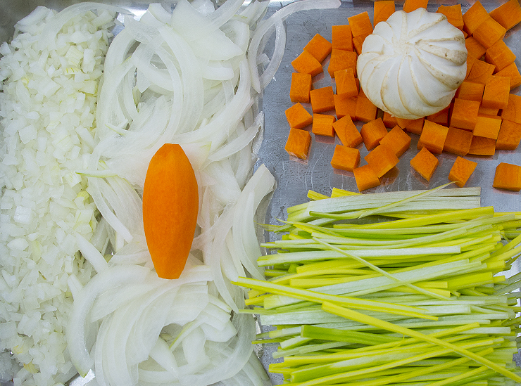 leeks, carrots, onions and a mushroom cut to fine perfection sit on a stainless steel tray