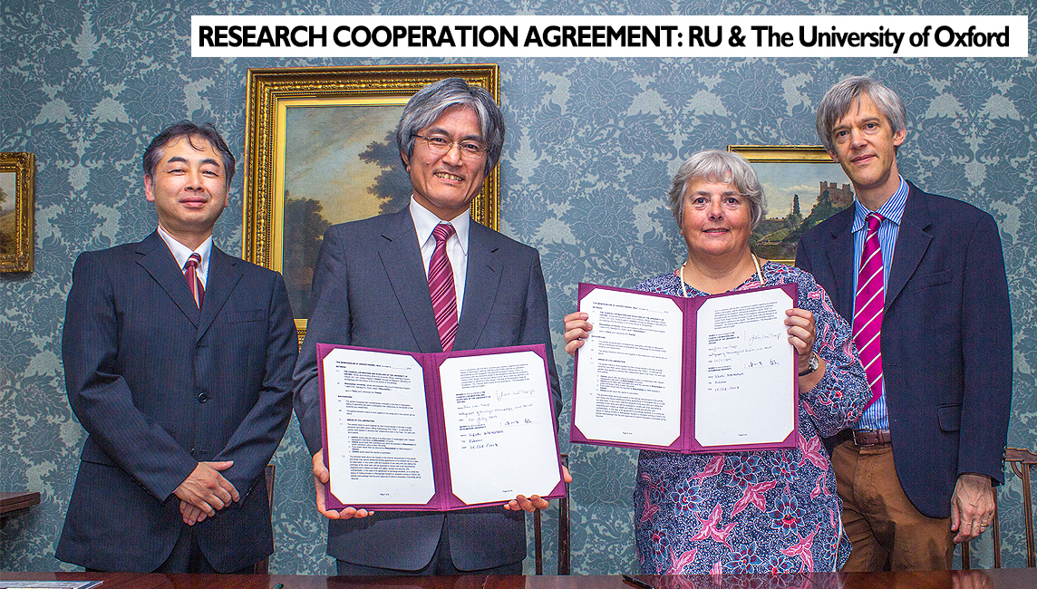 Agreement - Four leading research figures from Oxford and Ritsumeikan Universities pose in front of a wall decorated with old paintings and floral grasscloth wallpaper holding the signed agreements