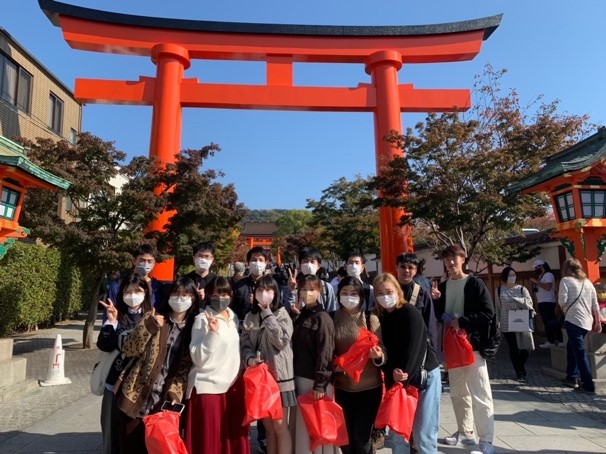 15 students posing in front of the giant orange entrance gate to a Shinto shrine