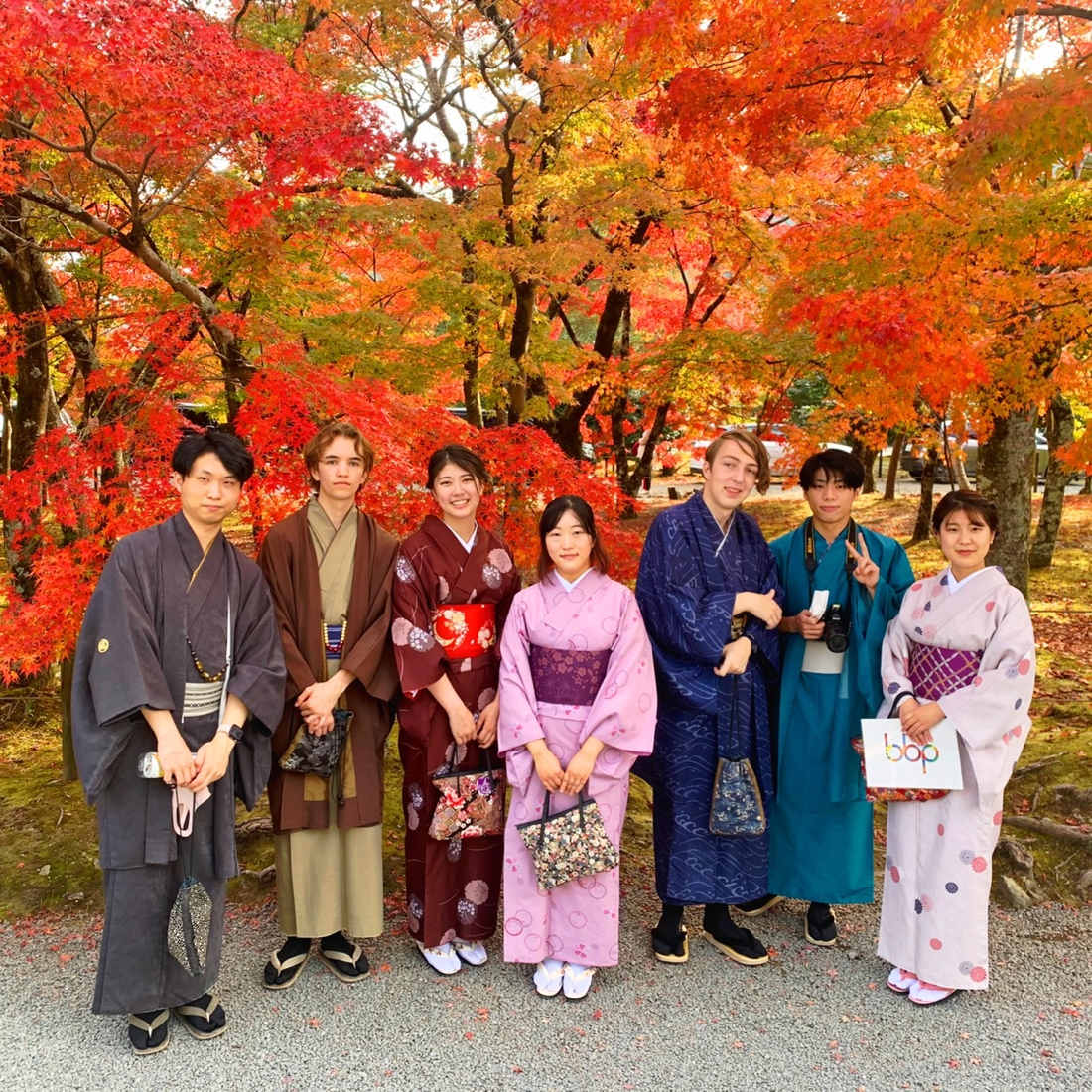 Students wear colorful kimonos in front of beautiful autumn foliage
