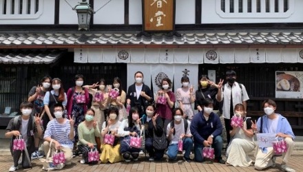 Group of students posing for a photo in front of a traditional Japanese building with white walls and a grey tile roof