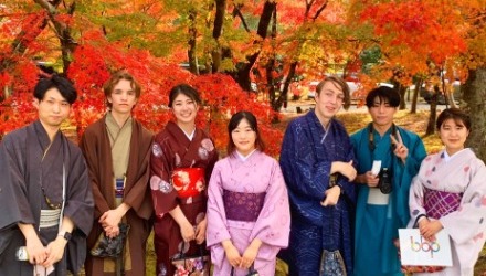 Students wear colorful kimonos in front of beautiful autumn foliage