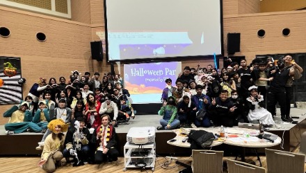 Group photo of students dressed for Halloween, gathered on top of a stage